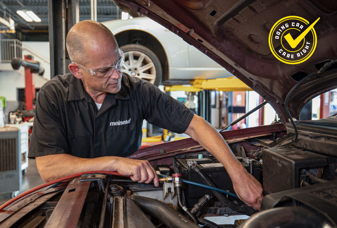 Meineke technician connecting A/C manifold gauges under the hood