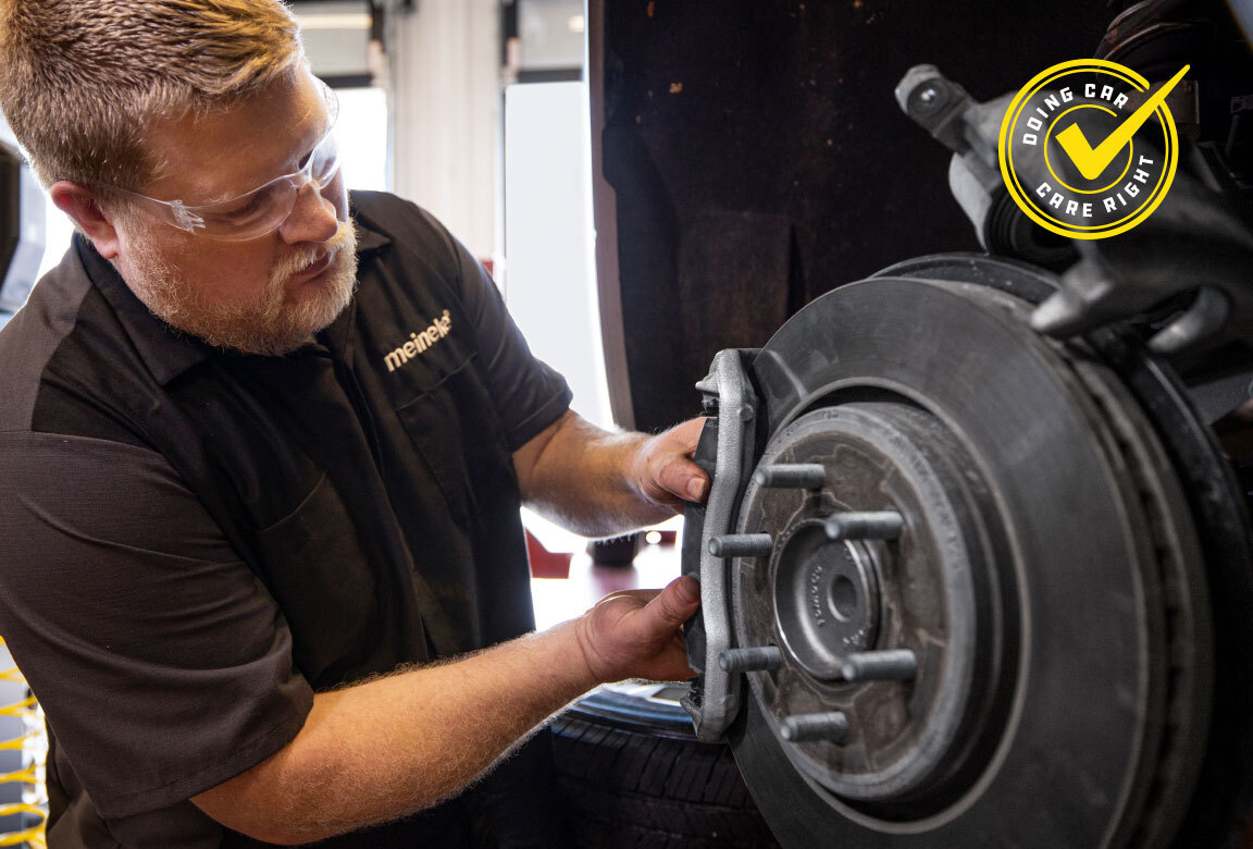 Meineke technician fitting a brake caliper and rotor